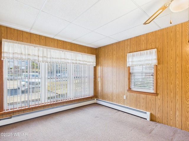 carpeted empty room featuring ceiling fan, baseboard heating, and wooden walls