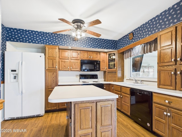 kitchen with a sink, light countertops, brown cabinets, black appliances, and wallpapered walls