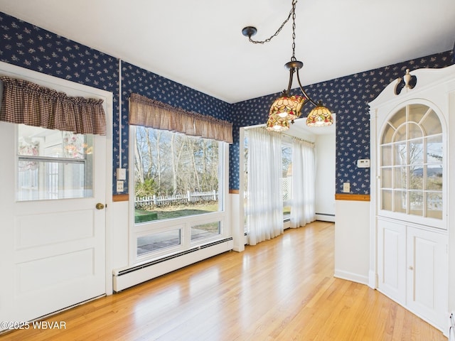 unfurnished dining area featuring a baseboard radiator, wood finished floors, baseboard heating, and wallpapered walls