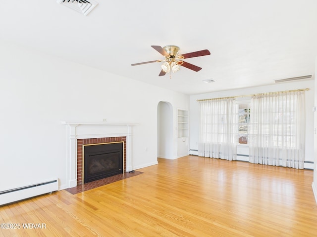 unfurnished living room featuring arched walkways, a fireplace, a baseboard radiator, visible vents, and wood finished floors