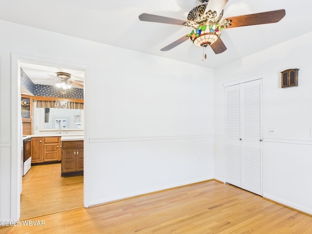 empty room featuring baseboards, a sink, a ceiling fan, and light wood-style floors