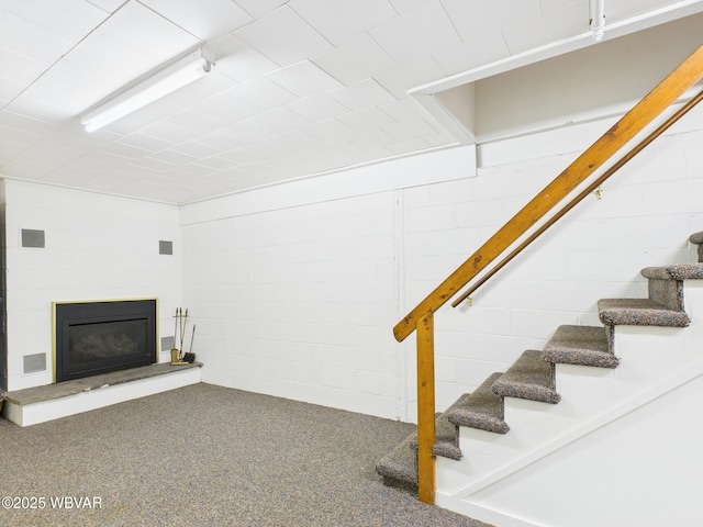 below grade area with visible vents, stairway, carpet, a glass covered fireplace, and concrete block wall