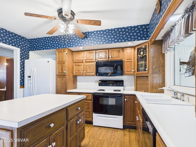 kitchen featuring light wood finished floors, light countertops, a sink, black appliances, and wallpapered walls