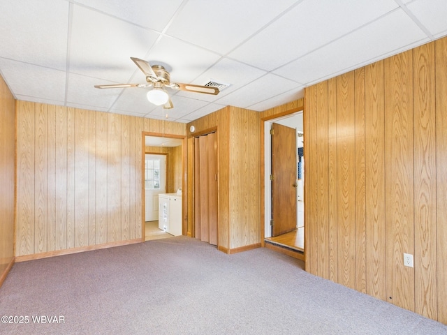 carpeted spare room with ceiling fan, a paneled ceiling, visible vents, and wooden walls