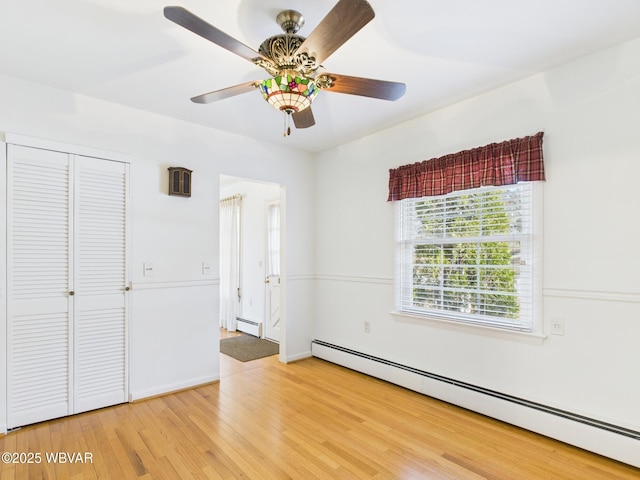 unfurnished bedroom featuring light wood finished floors, ceiling fan, a baseboard heating unit, and a closet