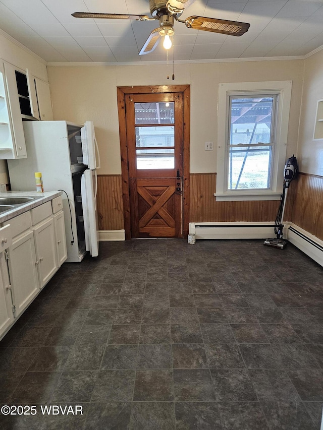 kitchen with white cabinetry, ceiling fan, crown molding, and wood walls