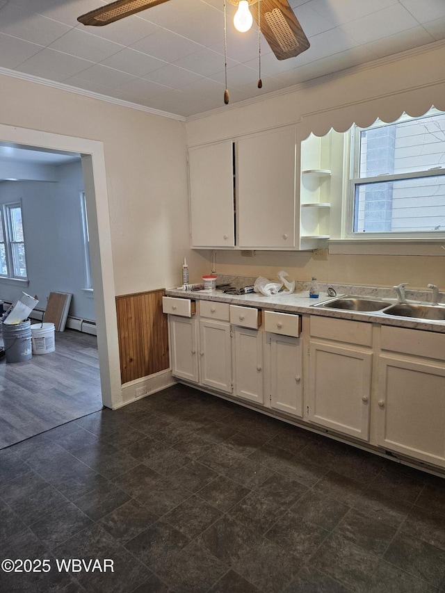 kitchen with a baseboard heating unit, sink, crown molding, white cabinetry, and wood walls