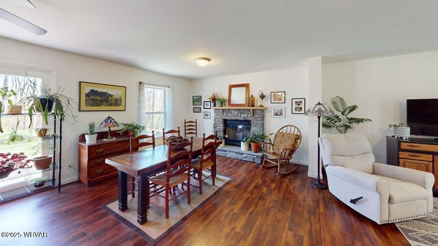 dining area featuring dark wood finished floors, baseboards, a wealth of natural light, and a stone fireplace
