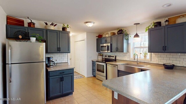 kitchen with a sink, decorative backsplash, a peninsula, pendant lighting, and appliances with stainless steel finishes