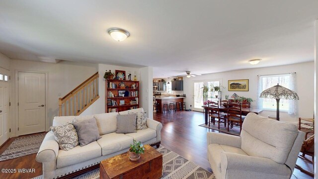 living area with stairs, a ceiling fan, and dark wood-type flooring