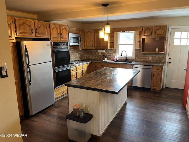 kitchen with appliances with stainless steel finishes, sink, a center island, dark hardwood / wood-style floors, and hanging light fixtures