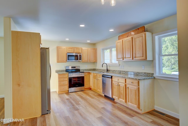 kitchen featuring light stone countertops, sink, light wood-type flooring, and stainless steel appliances