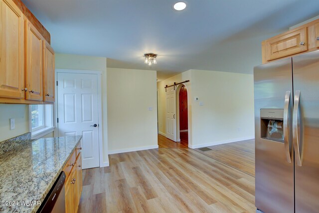 kitchen with a barn door, stainless steel fridge with ice dispenser, light stone counters, light brown cabinetry, and light wood-type flooring