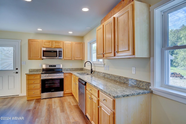 kitchen with light brown cabinetry, stainless steel appliances, sink, stone counters, and light hardwood / wood-style floors