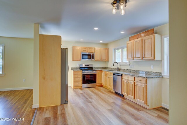 kitchen featuring light brown cabinets, light wood-type flooring, stainless steel appliances, and light stone counters