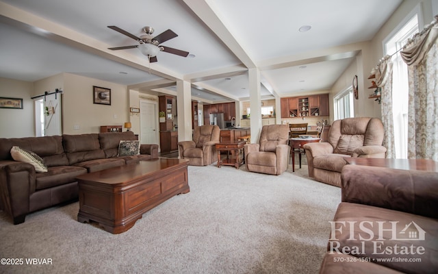 living room featuring beamed ceiling, a barn door, light carpet, and ceiling fan