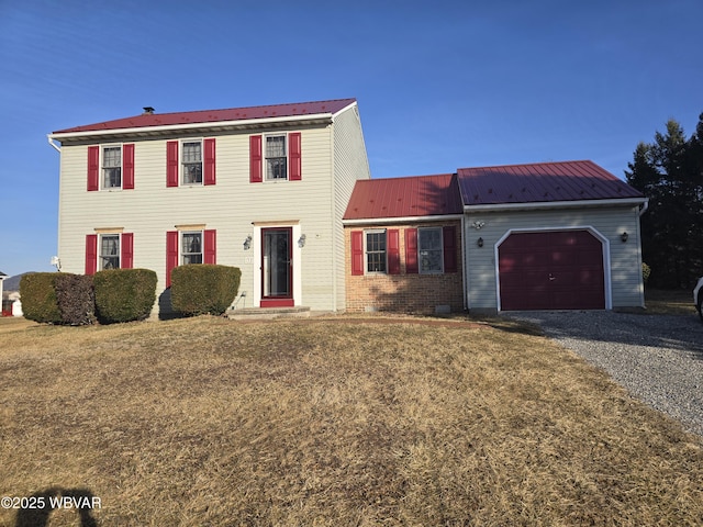 colonial home featuring a garage, brick siding, metal roof, and driveway