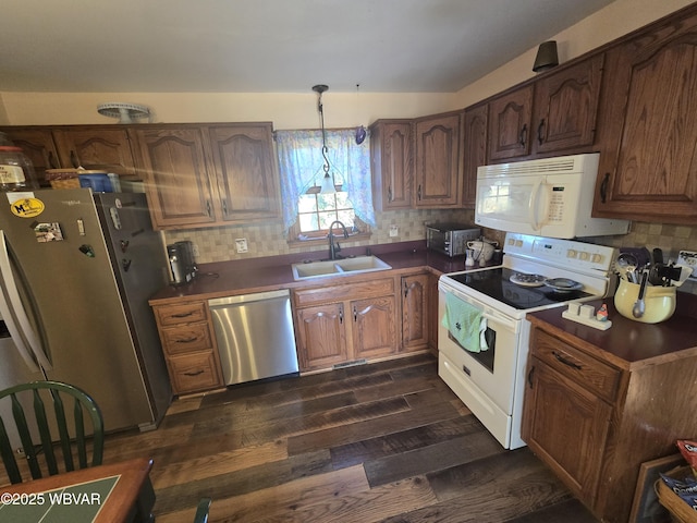 kitchen with dark countertops, tasteful backsplash, dark wood-type flooring, appliances with stainless steel finishes, and a sink