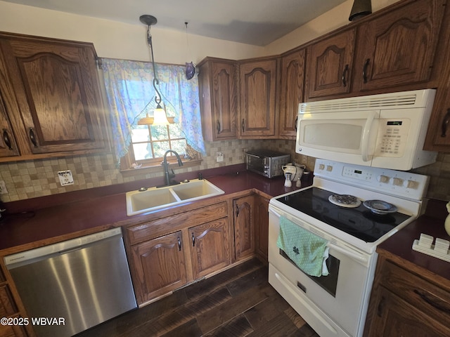 kitchen with white appliances, a sink, dark wood-type flooring, dark countertops, and backsplash