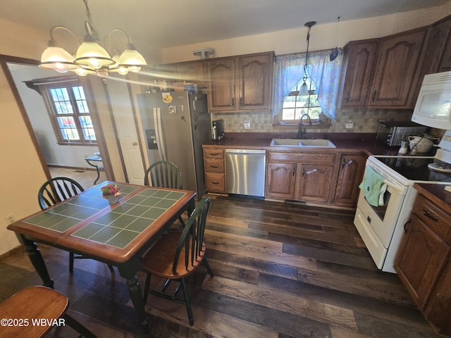 kitchen with dark wood-type flooring, decorative backsplash, appliances with stainless steel finishes, a notable chandelier, and a sink