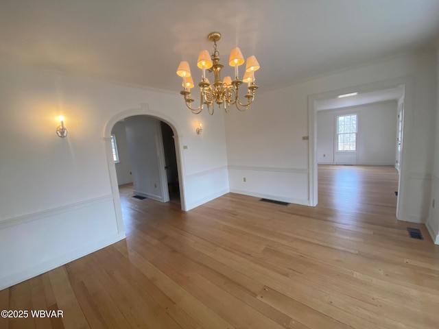 unfurnished dining area with arched walkways, light wood-style flooring, visible vents, and baseboards