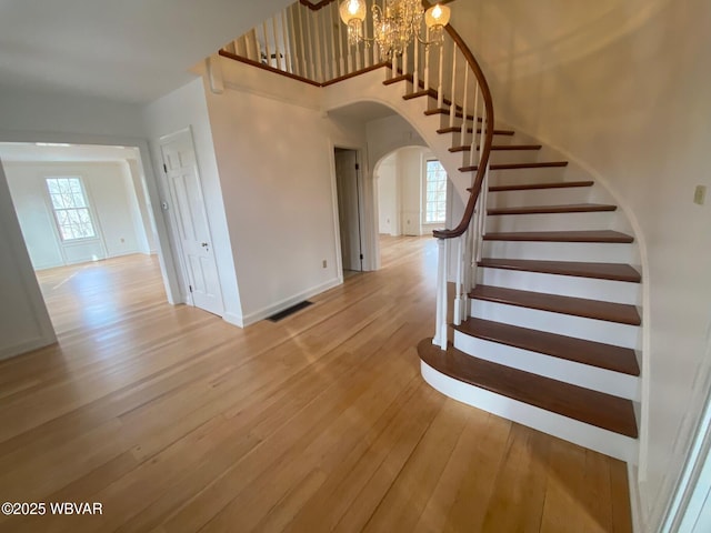 staircase featuring arched walkways, a notable chandelier, visible vents, baseboards, and hardwood / wood-style floors