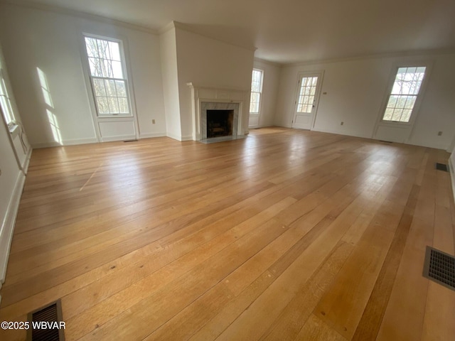 unfurnished living room with visible vents, ornamental molding, a high end fireplace, and light wood-style floors