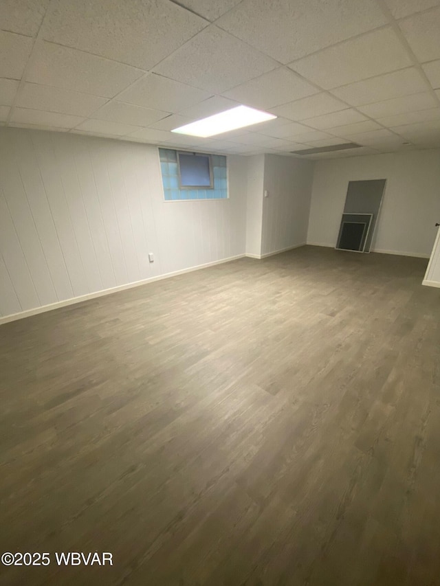 finished basement with dark wood-style floors, a paneled ceiling, and baseboards