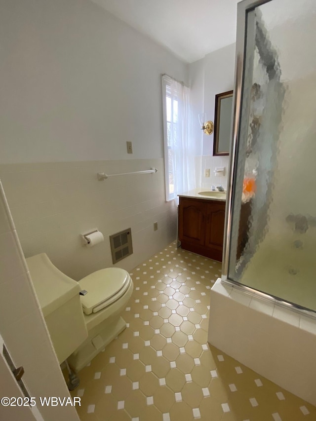 bathroom with toilet, visible vents, vanity, tile walls, and wainscoting