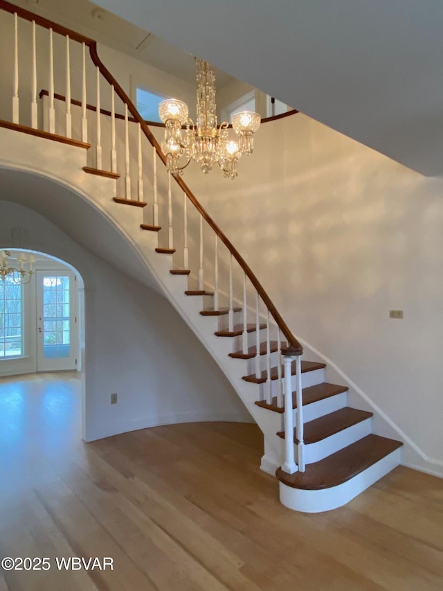 staircase with a towering ceiling, baseboards, a chandelier, and wood finished floors