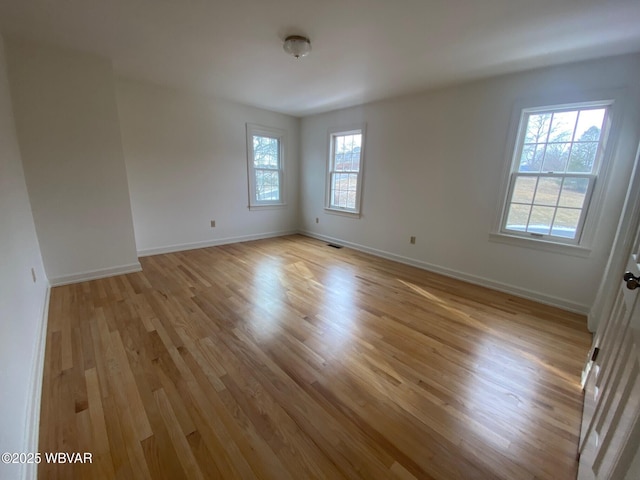 unfurnished room featuring light wood-type flooring, visible vents, and baseboards