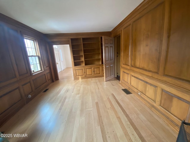 unfurnished living room with a decorative wall, visible vents, and light wood-style floors