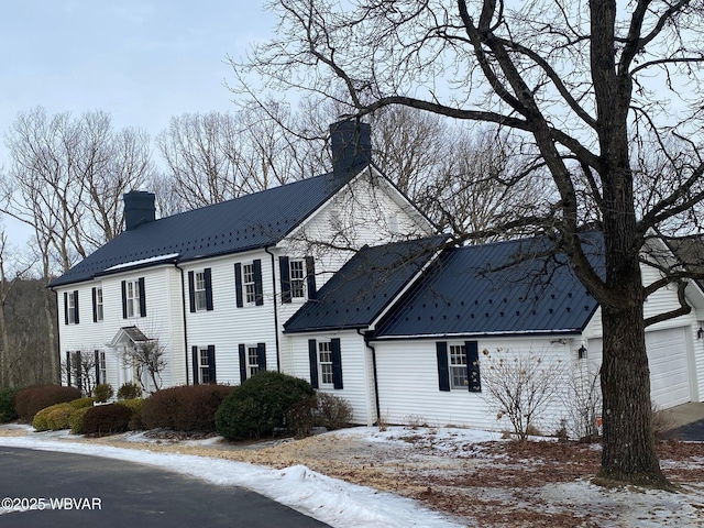 colonial house featuring a garage, metal roof, and a chimney