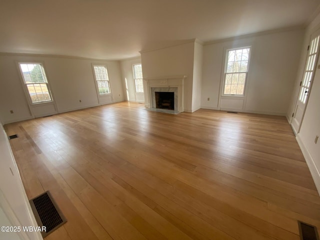 unfurnished living room featuring light wood finished floors, visible vents, ornamental molding, and a high end fireplace