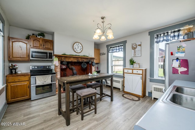 kitchen featuring pendant lighting, radiator, light hardwood / wood-style flooring, appliances with stainless steel finishes, and a chandelier