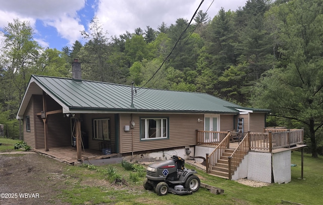 view of front facade featuring a chimney, a standing seam roof, metal roof, a wooden deck, and a forest view