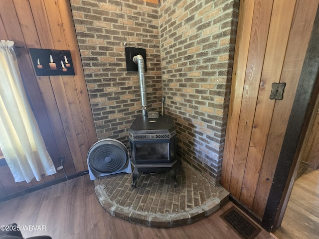 detailed view of a wood stove, brick wall, wood finished floors, and wooden walls