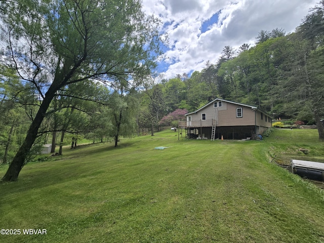view of green lawn featuring a view of trees and a deck