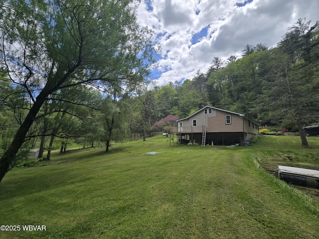 view of green lawn with a forest view and a wooden deck