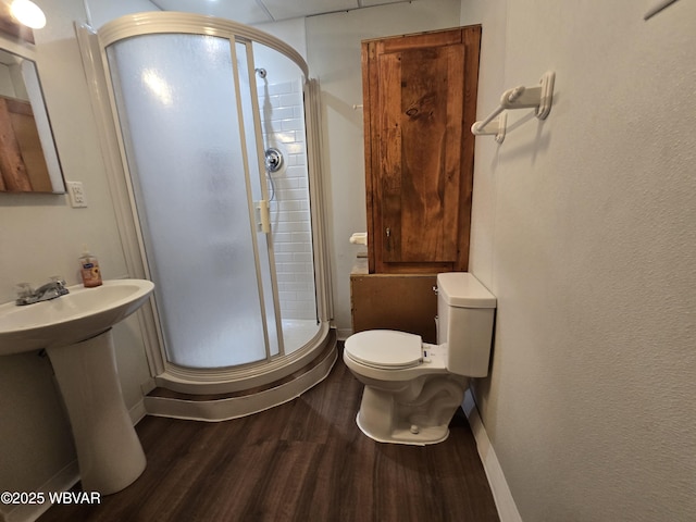 bathroom featuring wood finished floors, a stall shower, toilet, and baseboards