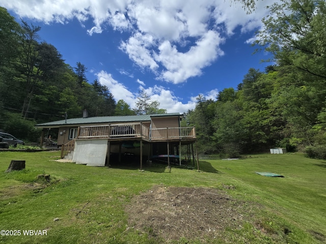 back of property featuring a wooden deck, a yard, metal roof, and an outdoor structure