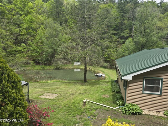 view of green lawn featuring a wooded view and a water view