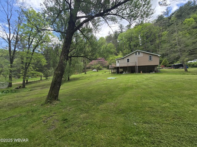 view of green lawn with a wooden deck and a view of trees