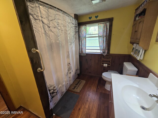 full bath featuring a wainscoted wall, hardwood / wood-style flooring, toilet, wood walls, and a shower with curtain