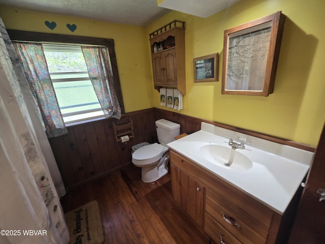 bathroom with wainscoting, wood finished floors, vanity, toilet, and wooden walls