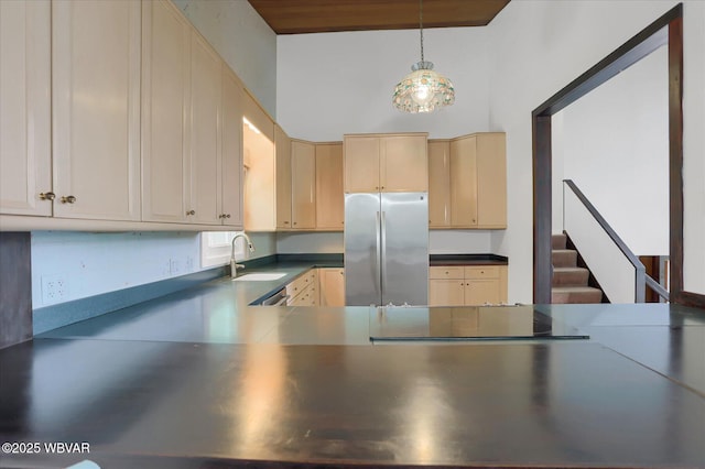 kitchen with dark countertops, hanging light fixtures, a sink, freestanding refrigerator, and light brown cabinets