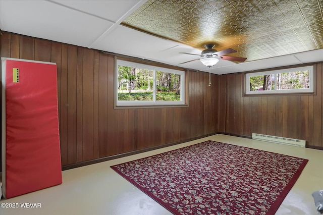 empty room featuring plenty of natural light, a ceiling fan, a baseboard heating unit, and wooden walls