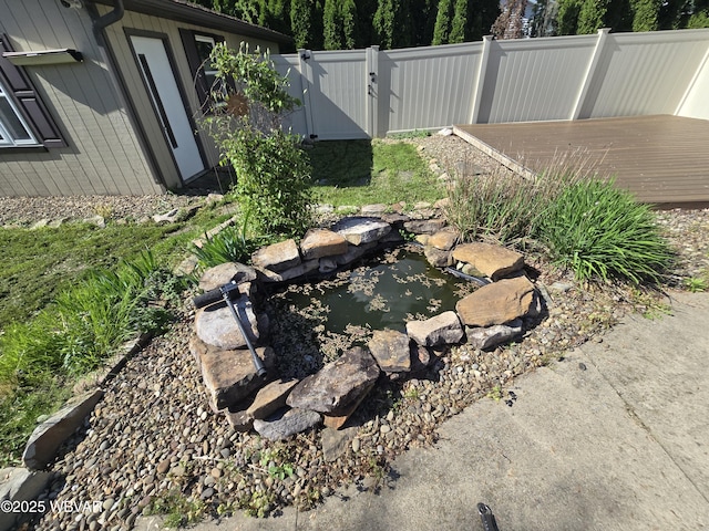 view of yard featuring fence, a garden pond, and a gate