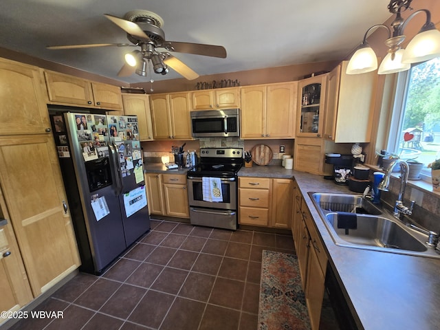 kitchen with stainless steel appliances, a sink, dark tile patterned flooring, light brown cabinetry, and ceiling fan