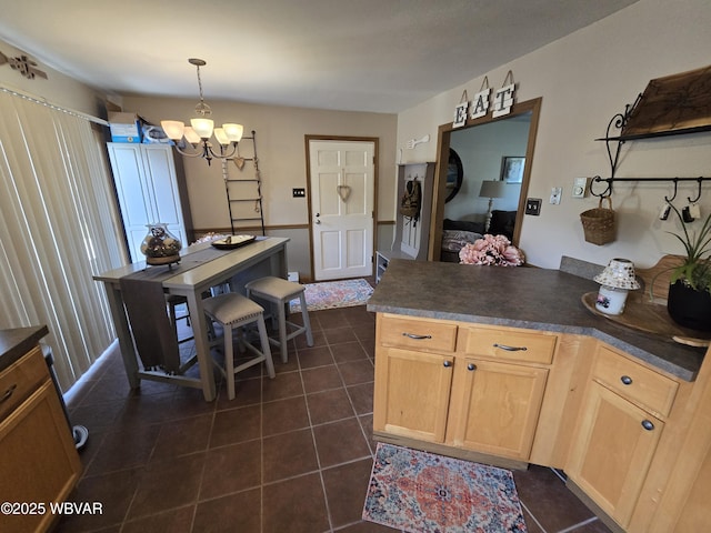 kitchen featuring a chandelier, dark countertops, a peninsula, dark tile patterned floors, and light brown cabinetry